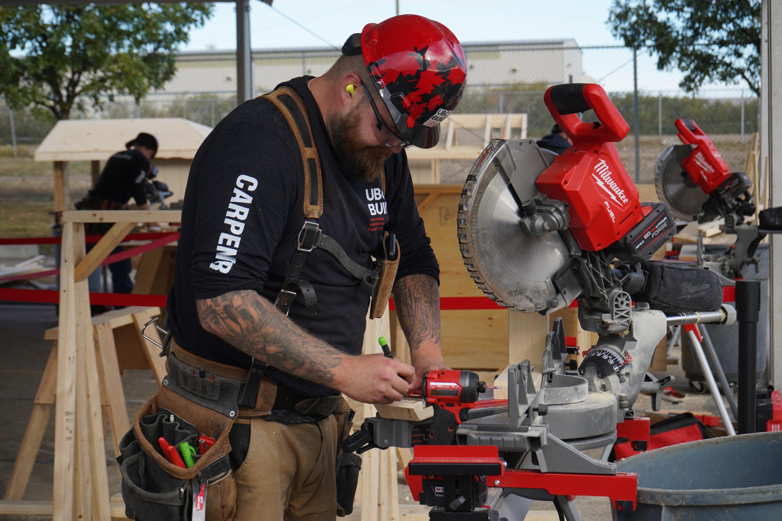 Construction worker with a red helmet using a miter saw at a woodworking job site with wooden structures